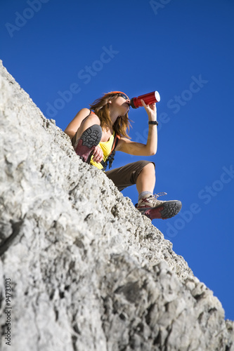 young woman drinking from flask on top of the mountain