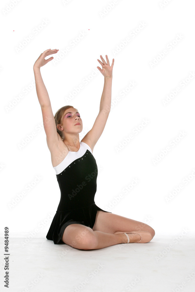 young ballerina in black sitting on floor with arms up