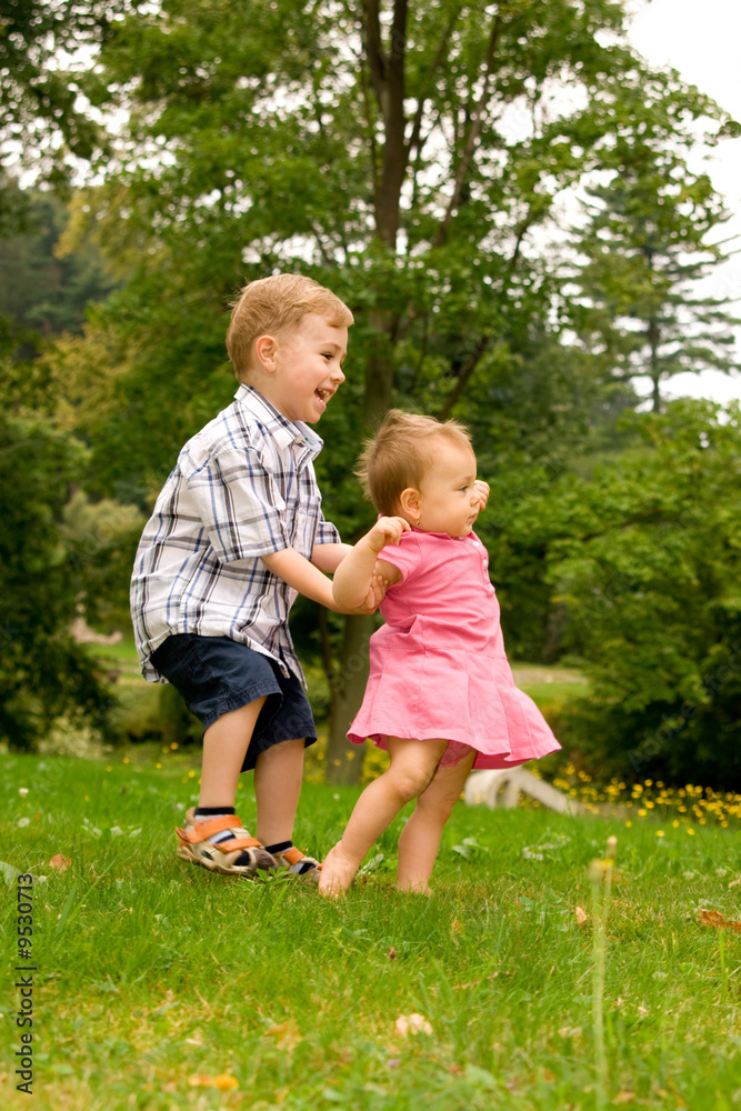Fototapeta premium A little boy playing with his toddler sister in the garden.