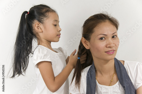 Asian Mom is having her hair braided by her daughter