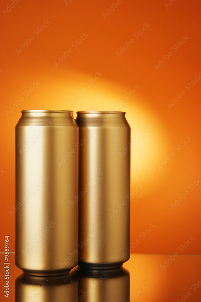 Two golden beer cans over orange background Two golden beer cans over orange background