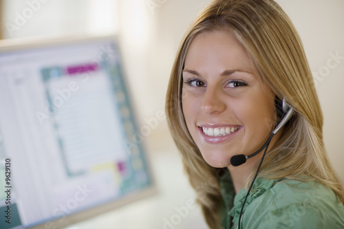 Smiling woman with headset and computer monitor photo