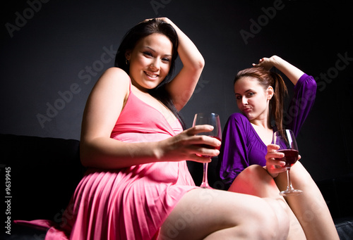 Two beautiful women dancing and drinking wine during a party