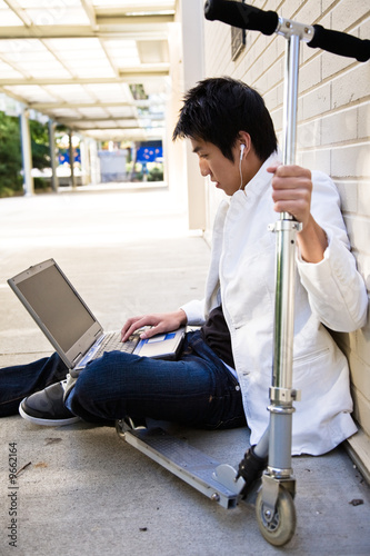 A young casual asian male using a laptop and listening to music