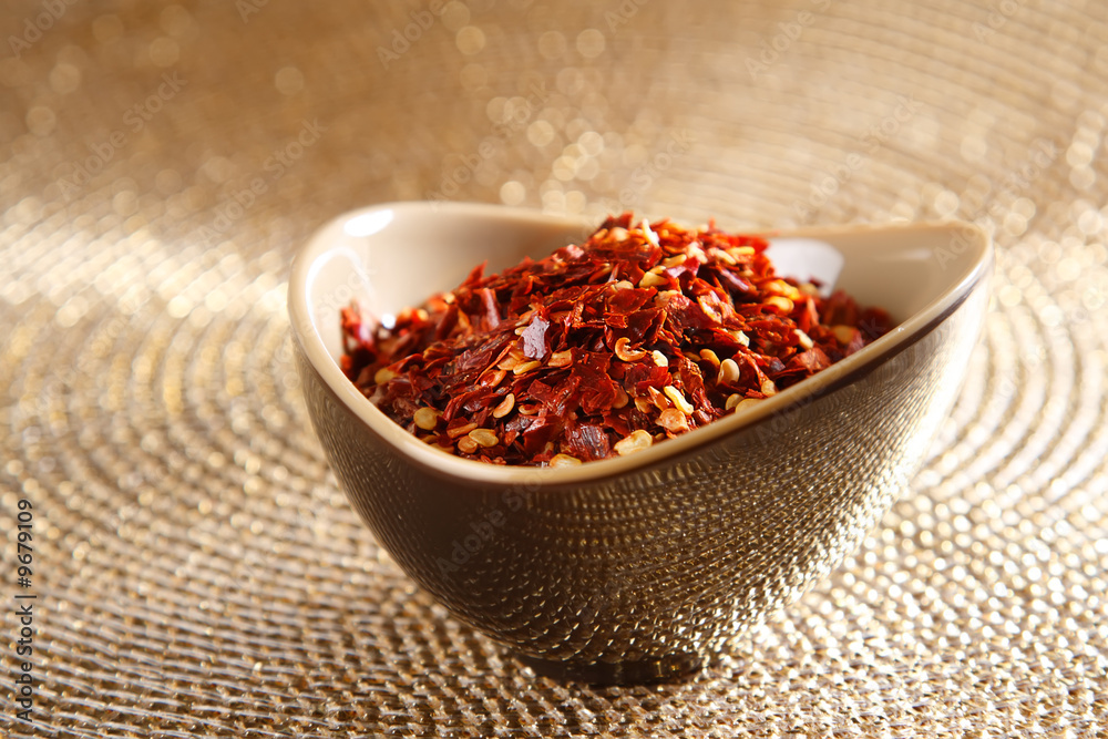crushed red hot chilli pepper in bowl on golden background crushed red hot chilli pepper in bowl on golden background