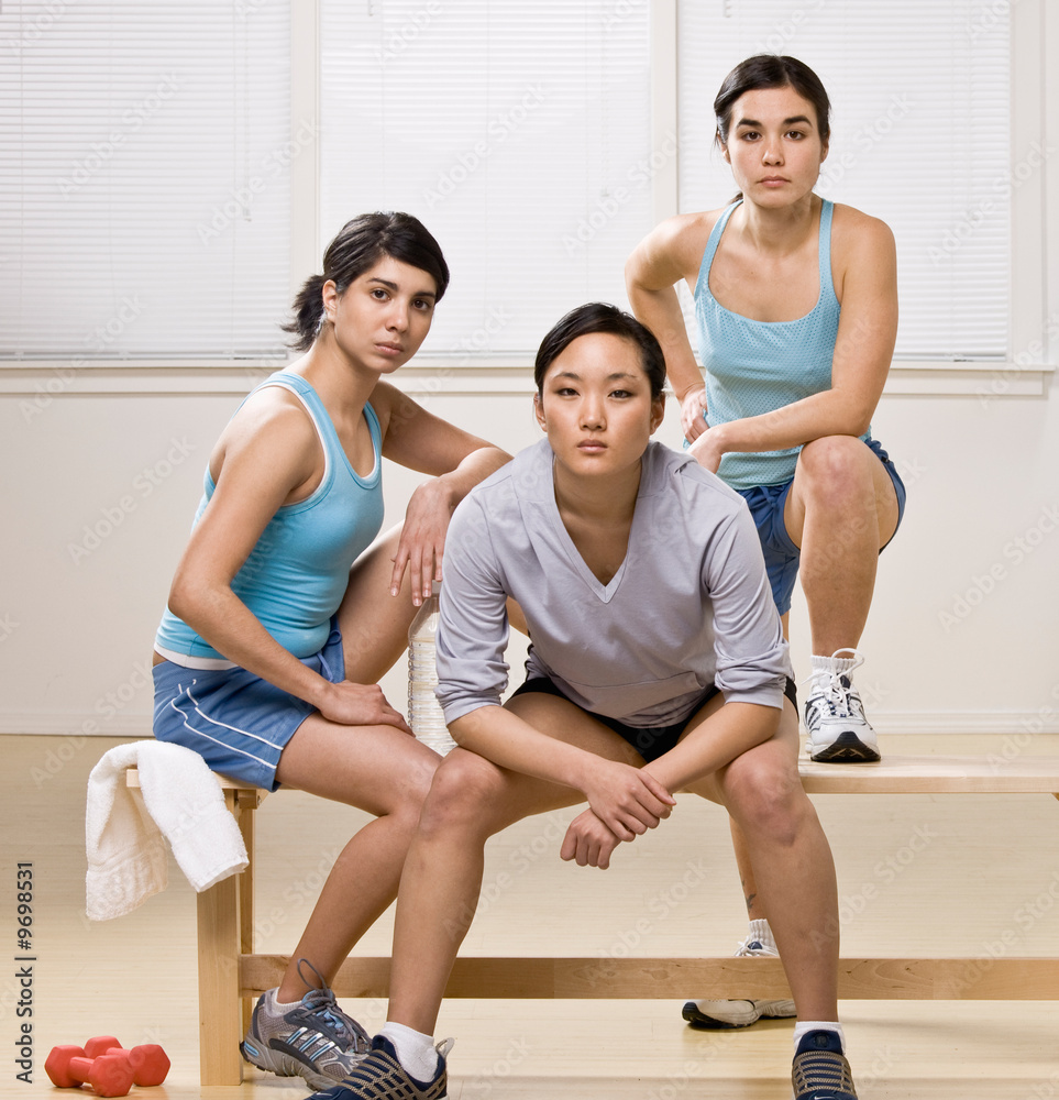 Friends in sportswear sitting on bench in health club