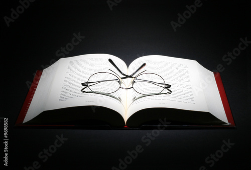 open book with a pair of eye glasses on dark background.