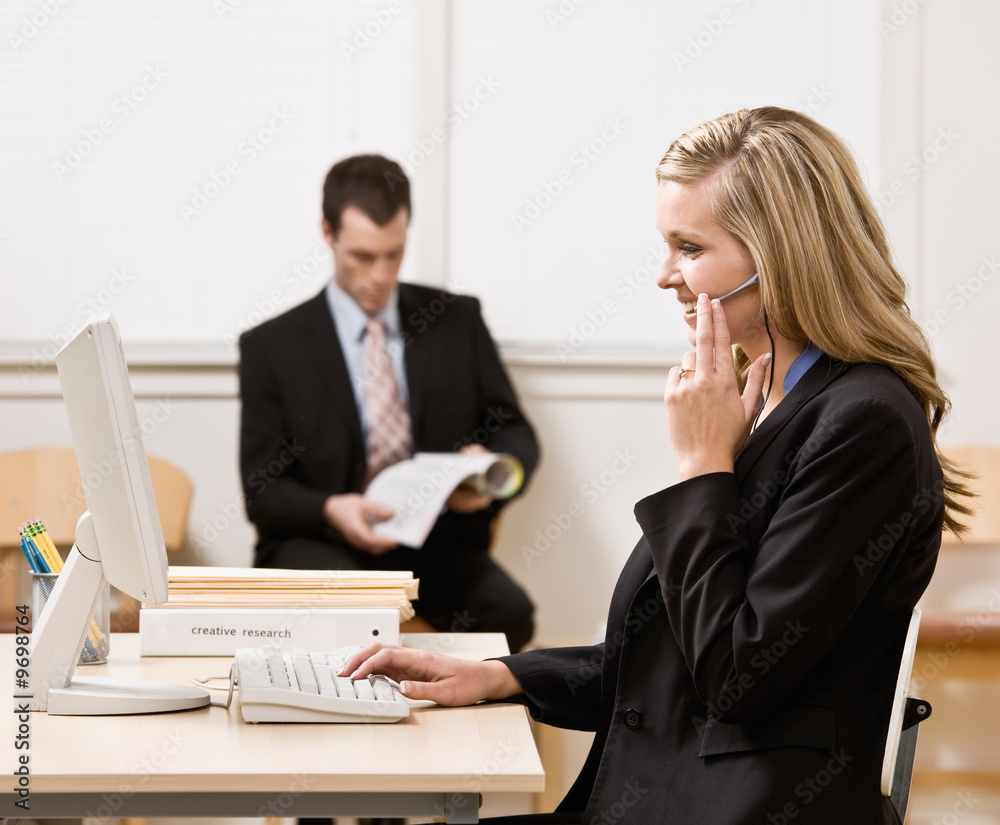 Businesswoman talking on headset with co-worker in background