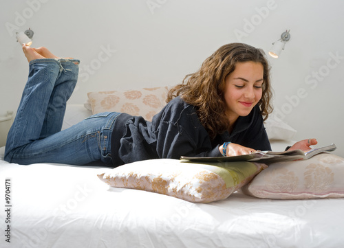 teenager girl lying in bed reading a magazine