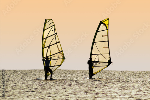 Silhouettes of two windsurfers on waves of a gulf