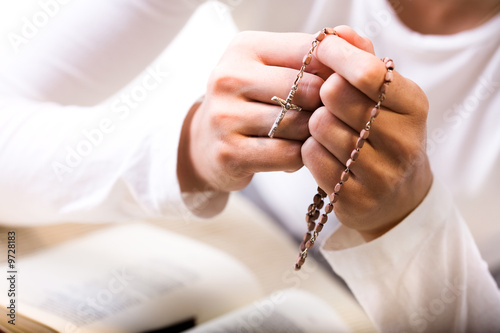 Christian believer praying to God with rosary in hand.