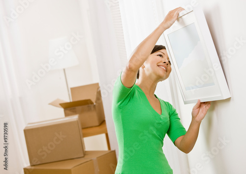 Happy woman moving into new home hanging picture on wall photo