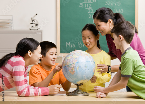 Teacher and students viewing globe in geography classroom