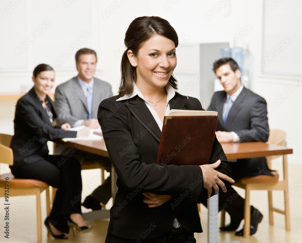Confident businesswoman with notebook and co-workers Confident businesswoman with notebook and co-workers