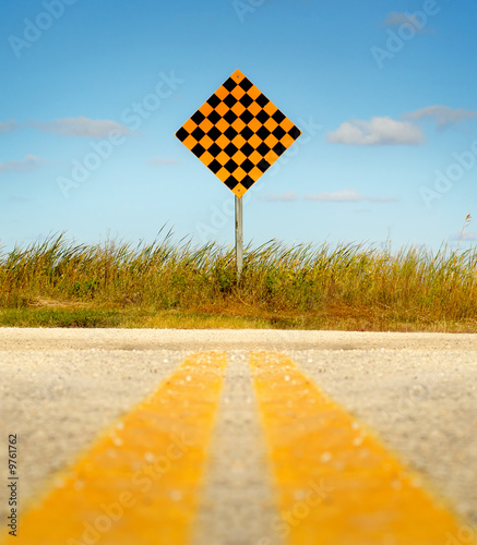 Paved road leading to dead end sign against a blue sky.
