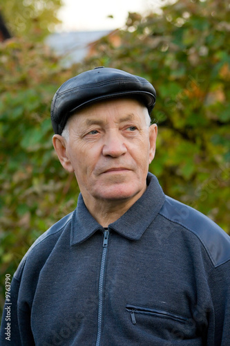 Portrait of the elderly man in a cap against the nature