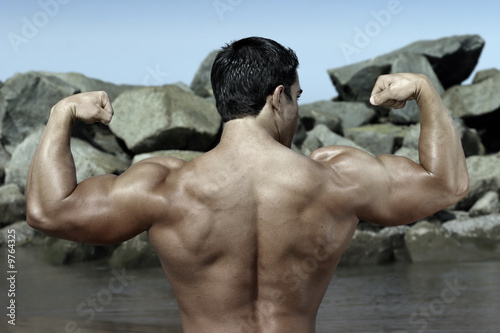 back of a bodybuilder flexing by some rocks on the beach photo