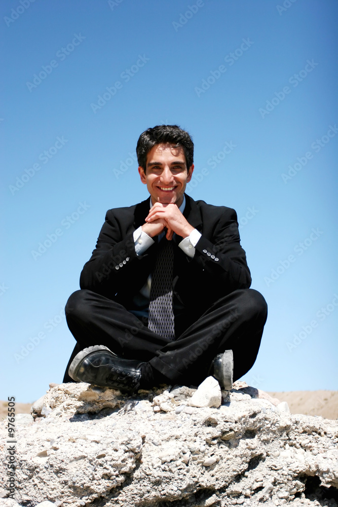 Businessman in black suit sitting on the rocks Businessman in black suit sitting on the rocks