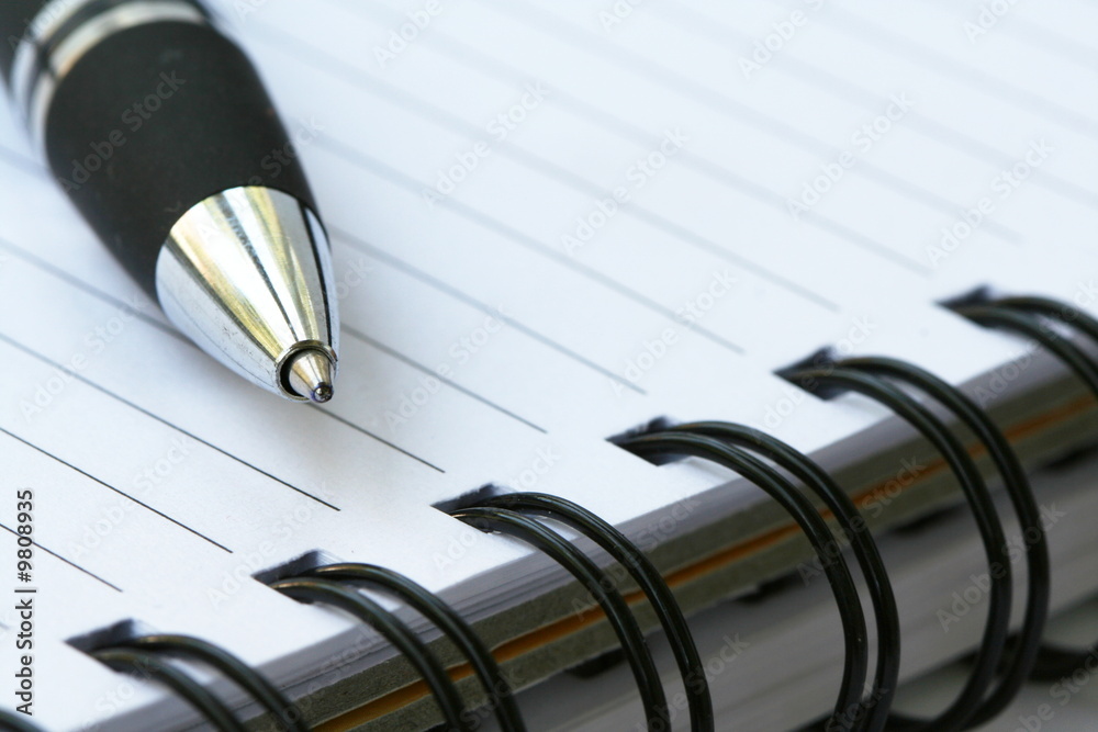 Silver-blue pen lying on opened notebook Silver-blue pen lying on opened notebook