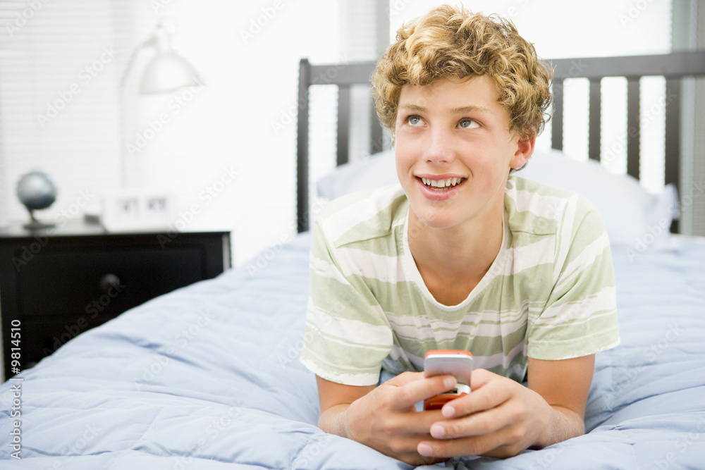 Teenage Boy Lying On Bed Using Mobile Phone