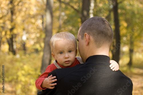 Young man takes his crying sun in his arm in autumn park