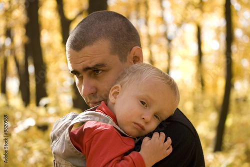 Young man takes his little son in his arms in autumn park