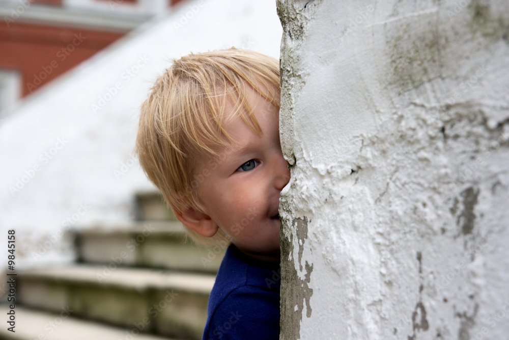 Child looks out from the wall and smiles Child looks out from the wall and smiles