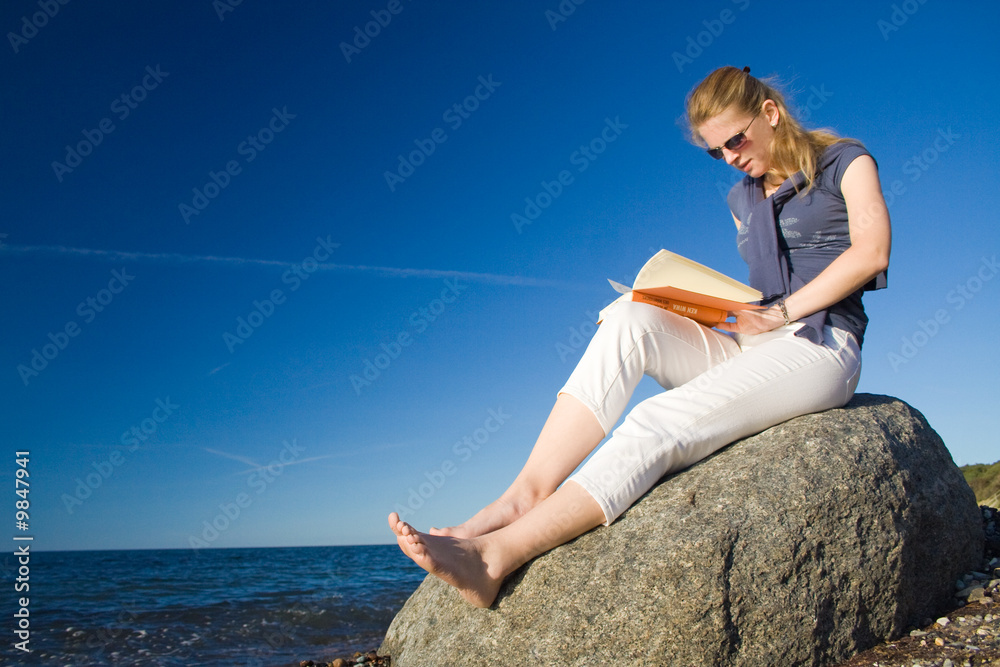 Frau am Strand liest ein Buch