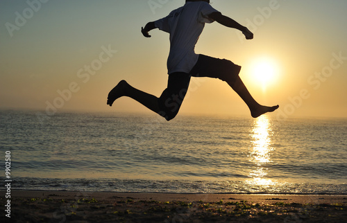 Young boy jumping on beach at sunrise