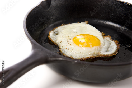 A fried egg in a black iron skillet on a white background,