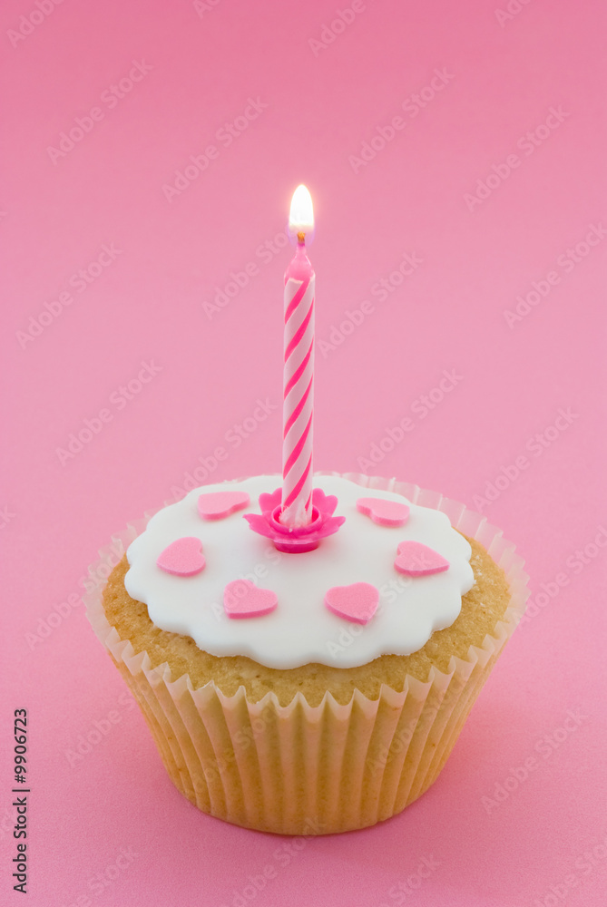 Single cupcake with pink lit candle in a pink setting