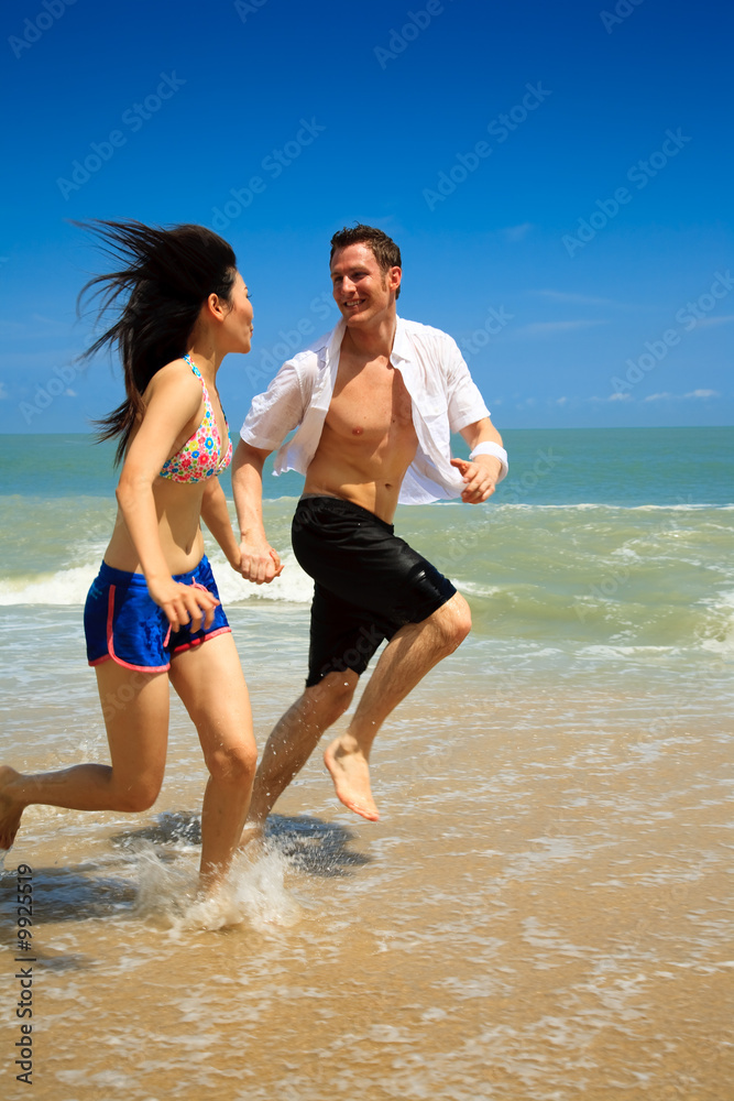 Couple running on beach holding hands smiling Couple running on beach holding hands smiling