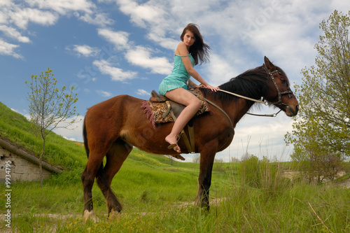 A beautiful girl in a blue dress riding a horse.