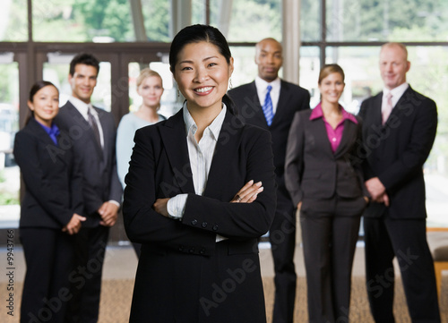 Confident Asian businesswoman posing in front of co-workers