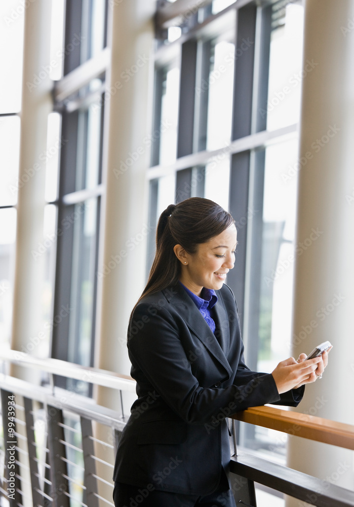 Businesswoman leaning on railing in office and text messaging Businesswoman leaning on railing in office and text messaging