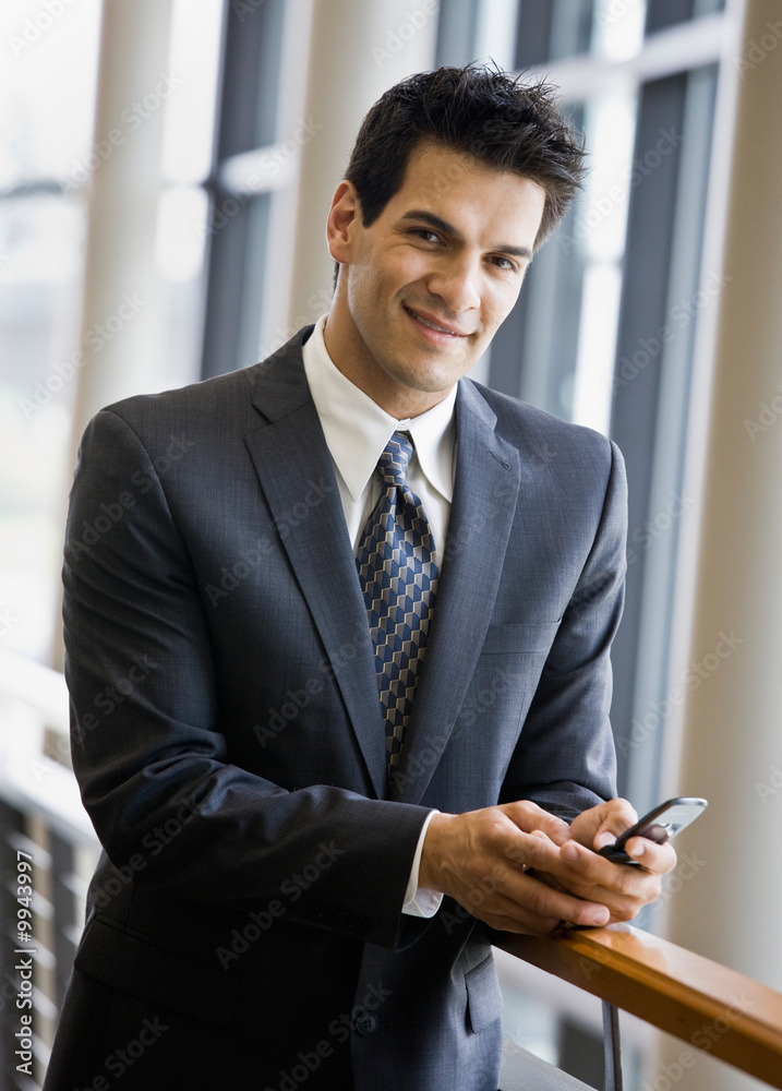 Businessman text messaging on cell phone in office lobby Businessman text messaging on cell phone in office lobby