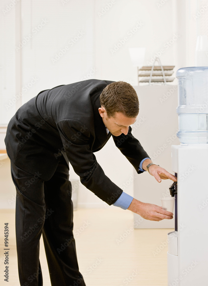 Thirsty businessman filling cup from water cooler