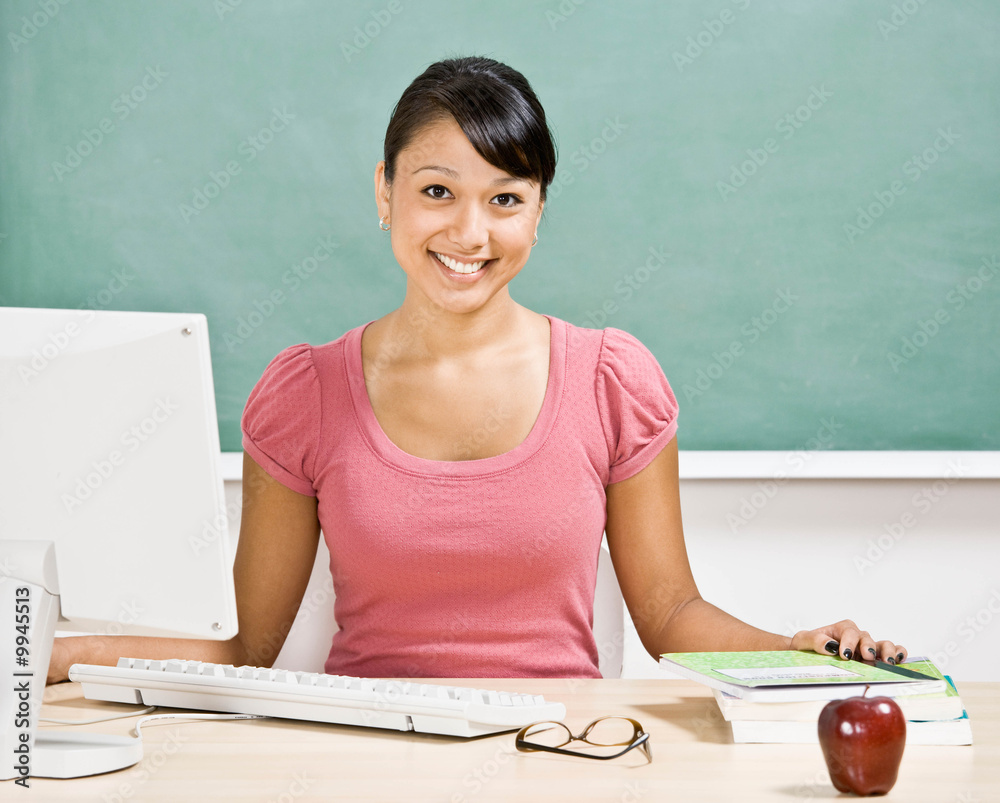 Teacher sitting at desk with computer in school classroom Teacher sitting at desk with computer in school classroom