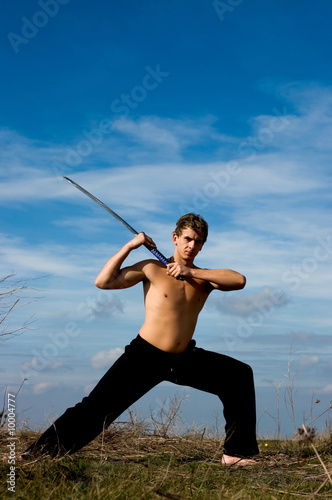 Young handsome man with samurai sword against blue sky.