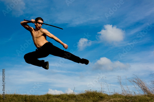 Young handsome man with samurai sword jumping