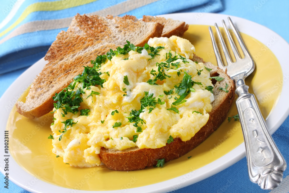 Scrambled eggs garnished with parsley, with sourdough toast.