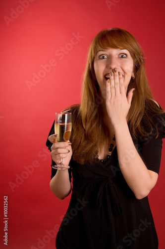 Surprised girl with champagne glass isolated on red background