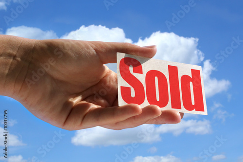 female hand holding sold card against sky,