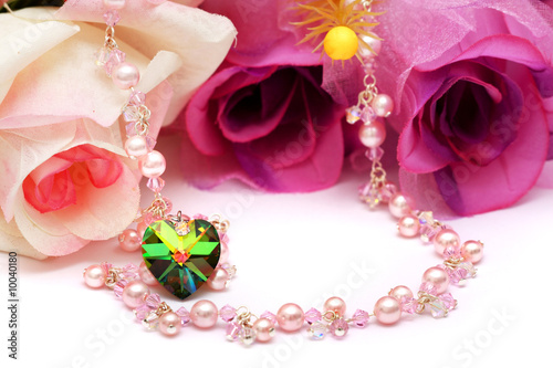 A heart shape bead and pink necklace put with flowers.