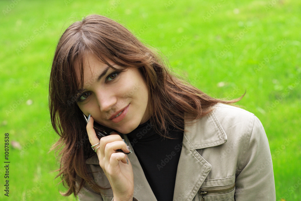 Beautiful young girl with a phone, over green grass background Beautiful young girl with a phone, over green grass background
