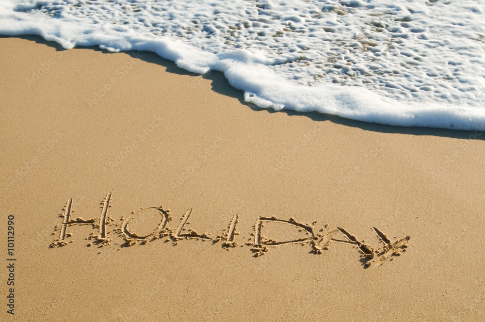 Fototapeta premium 'holiday' written onto sand surface about to be washed away