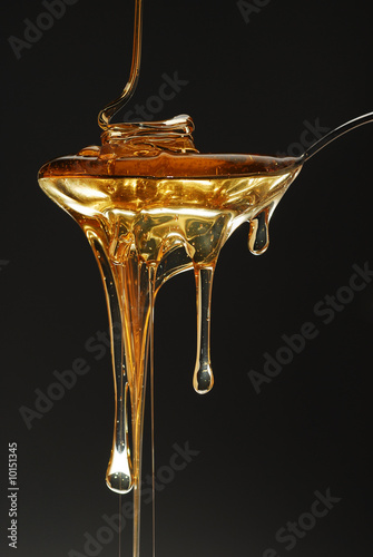 Leinwand Poster Golden honey spilling on dark background stock photo