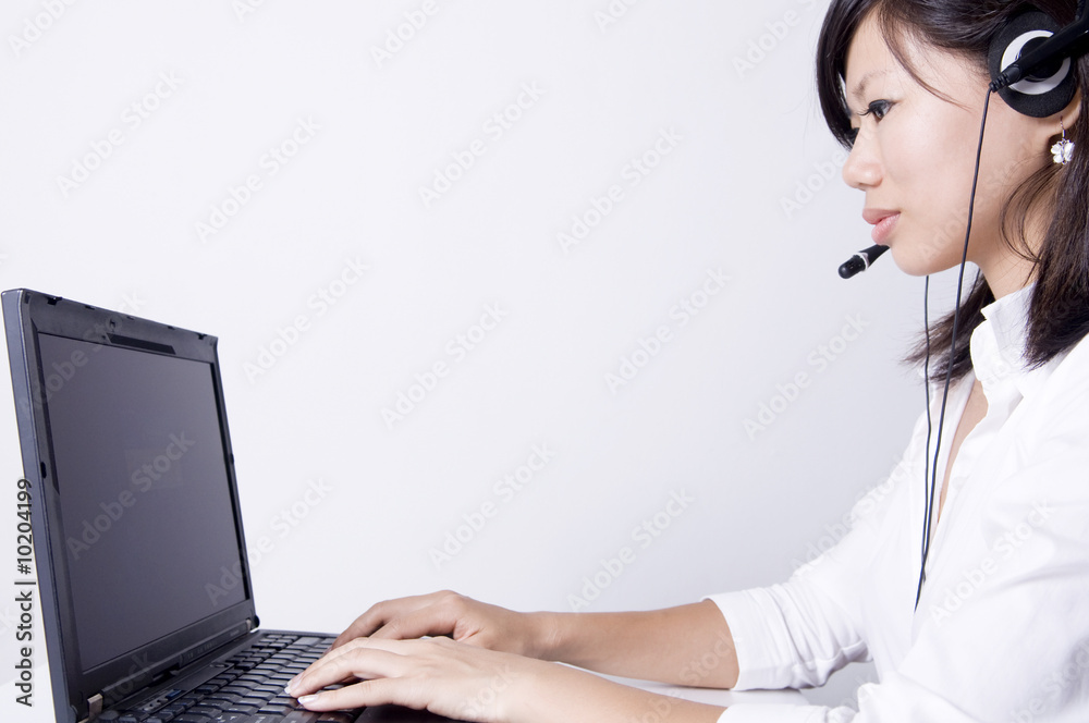Asian consultants with headsets working on laptop computer . Asian consultants with headsets working on laptop computer .