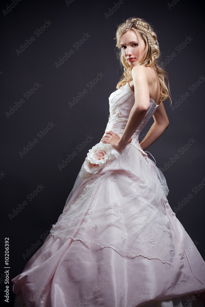 Beautiful blond bride wearing wedding dress posing on gray