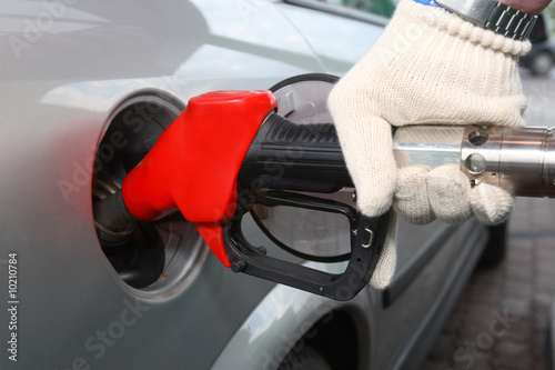 Bright red gas pump inserted into an automobile gasoline tank